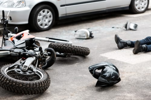 Image of motorcycle accident with motorcycle on it's side and rider laying on the ground with only his legs appearing in image